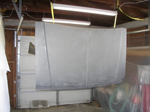 1987 Ford Bronco - Car hood prepared for painting, hanging in a garage with fluorescent lights overhead.