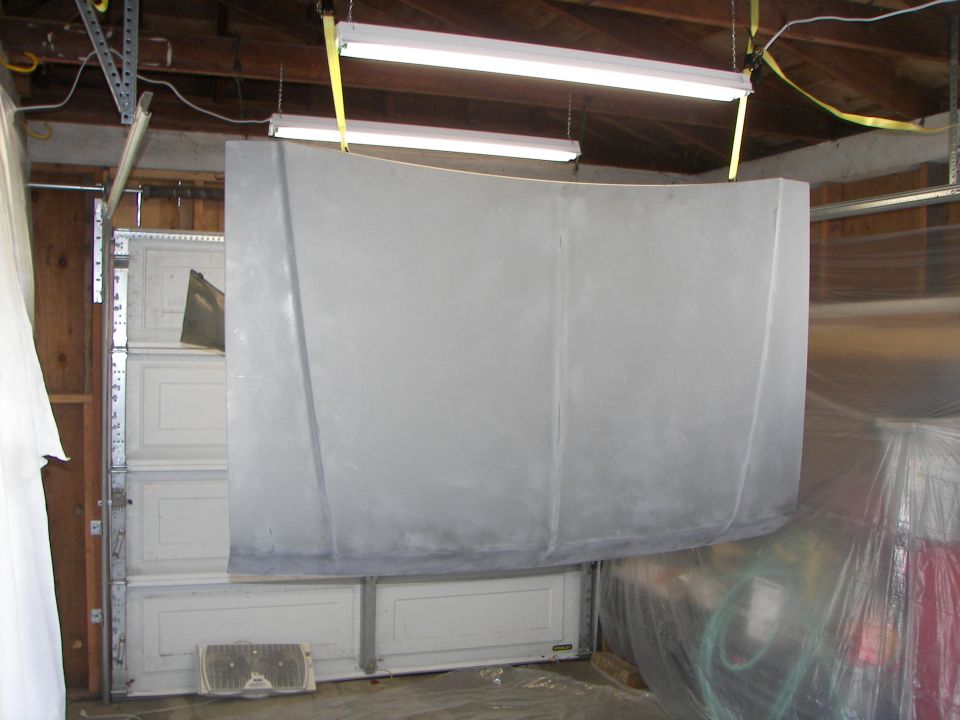 Gray car hood hanging in a garage, suspended by yellow straps