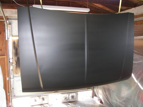 1987 Ford Bronco - A dark gray hood hangs in a garage, suggesting it is undergoing repair or painting.