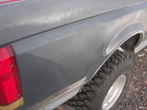 1987 Ford Bronco - The rear quarter panel of a vehicle shows some wear and a large off-road tire is visible.