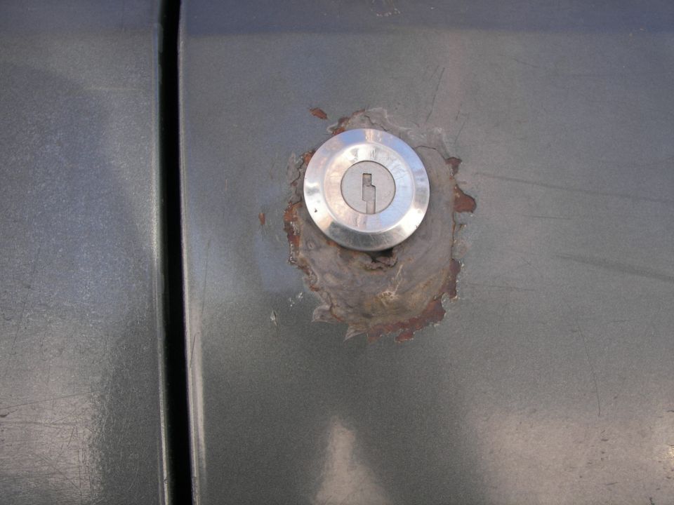 Gray vehicle door with a rusted lock cylinder, close-up view