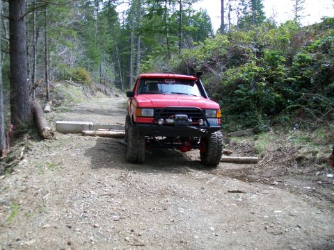 1991 Ford Bronco - Red 1991 Ford Bronco navigating an obstacle on a forest trail.