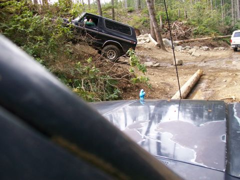 1991 Ford Bronco - A black Ford Bronco navigates a challenging off-road trail, with another vehicle visible in the distance.