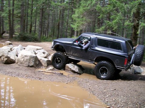 1991 Ford Bronco - Ford Bronco tackling an off-road obstacle course in a wooded area.