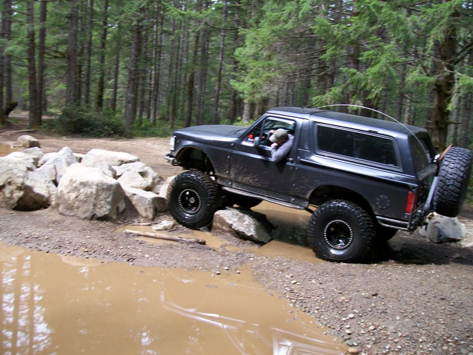 1991 Ford Bronco navigating a muddy trail with large rocks