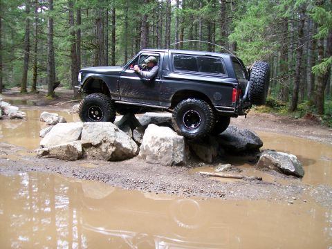 1991 Ford Bronco - This 1991 Ford Bronco is tackling a challenging off-road trail with large rocks and muddy water.