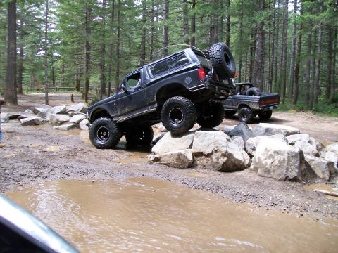 1991 Ford Bronco - A black 1991 Ford Bronco tackles an obstacle course of rocks and mud, with another truck visible in the background.