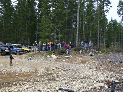 1991 Ford Bronco - A group of people stand around several parked vehicles in a wooded area.