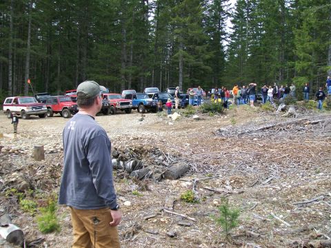 1991 Ford Bronco - A group of off-road enthusiasts and their vehicles are gathered in a clearing surrounded by trees.
