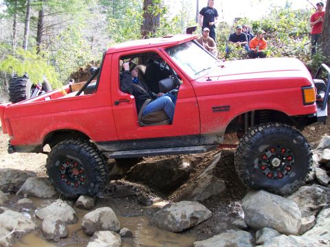 1991 Ford Bronco - This modified SUV is shown off-roading over a challenging obstacle course of rocks and mud.