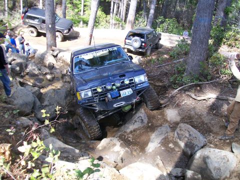 1991 Ford Bronco - A blue 1991 Ford Bronco tackles a challenging rocky obstacle course during an off-road event.