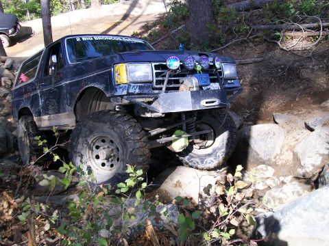 1991 Ford Bronco - Off-road Bronco tackling a tough rock obstacle. The grille indicates it's likely from the late 1980s.