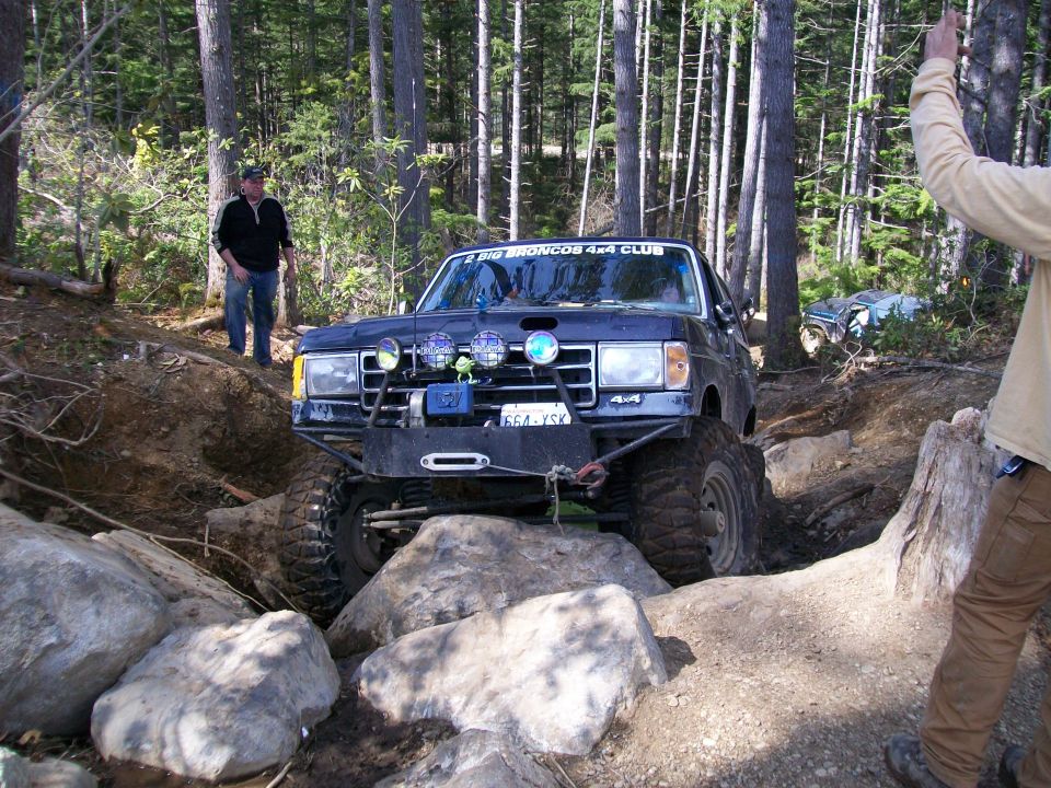 1991 Ford Bronco navigating rocks on a trail, with another vehicle visible in the background