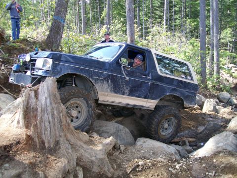 1991 Ford Bronco - A modified Ford Bronco tackles a challenging off-road course with large rocks and trees.