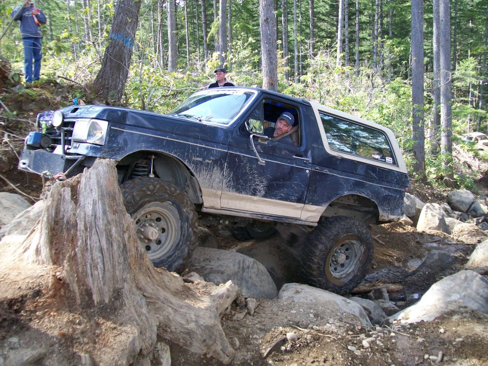 Dark blue Ford Bronco with a tan stripe, lifted suspension, and off-road tires navigating a rocky trail