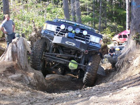1991 Ford Bronco - A modified 1991 Ford Bronco tackles a challenging off-road course, with other vehicles visible in the background.