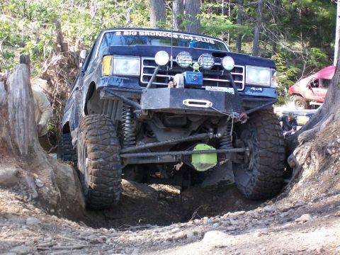 1991 Ford Bronco - This modified off-road vehicle is navigating a challenging trail with a large tree stump and other vehicles nearby.