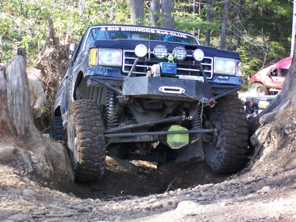 Dark blue off-road vehicle with large tires navigating a ditch, another red vehicle visible behind it