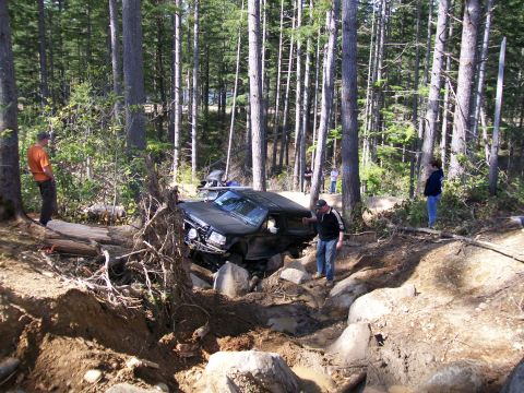 1991 Ford Bronco - A black SUV is stuck in a challenging off-road terrain, surrounded by trees and large rocks.