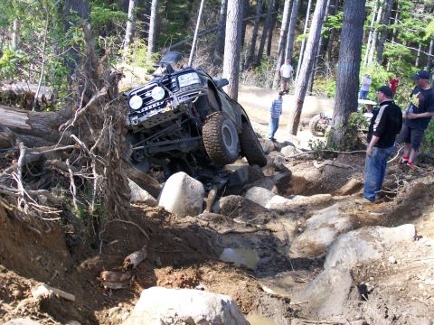 1991 Ford Bronco - A group of people watch as an off-road vehicle attempts to navigate a challenging rocky and muddy course.