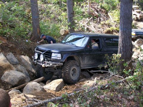1991 Ford Bronco - A black Ford Bronco is shown navigating a difficult, rocky off-road trail in a wooded area.