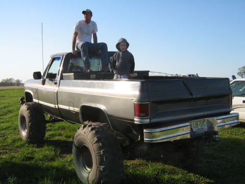 1990 Ford Bronco - Two people relax in the bed of a lifted pickup truck on a sunny day.
