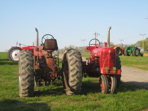 1990 Ford Bronco - Two vintage red tractors are parked side-by-side on a grassy field under a clear blue sky.