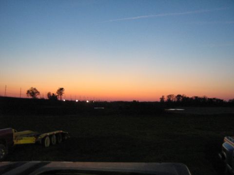 1990 Ford Bronco - A trailer and part of a truck bed are visible in the foreground as the sun sets over a rural landscape.
