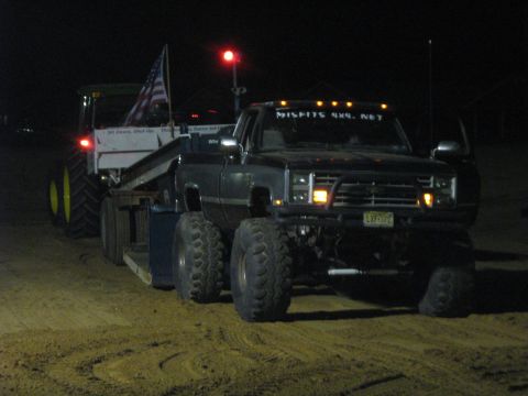 1990 Ford Bronco - Pickup truck tows a tractor at night, displaying 'MISFITS 4X4. NET' on its windshield.