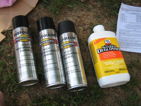 1990 Ford Bronco - Supplies for a painting project are laid out on the grass, including spray paint and a liquid deglosser.