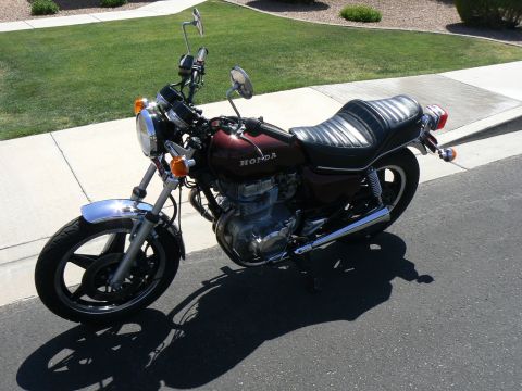1978 Ford Bronco - A maroon Honda motorcycle is parked on the side of a road with a grassy area in the background.