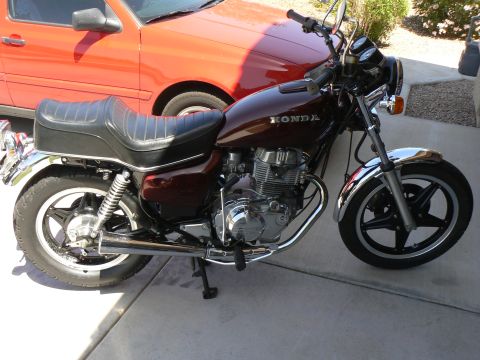 1978 Ford Bronco - A maroon Honda motorcycle is parked next to a red car in a driveway.