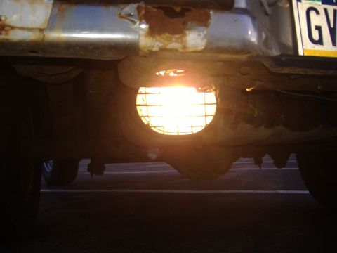 1988 Ford Bronco - Close-up of the rear of a vehicle, showing a rusty bumper and a lit round lamp.