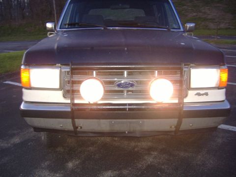 1988 Ford Bronco - Frontal view of a dark SUV, a brush guard with two large fog lights and a '4x4' badge.
