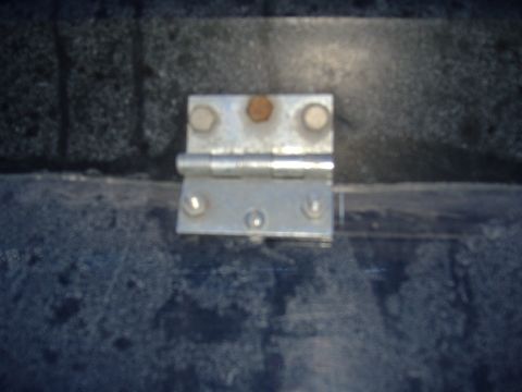 1988 Ford Bronco - A close-up view of a metal hinge, likely a replacement part, with visible bolts and some rust.