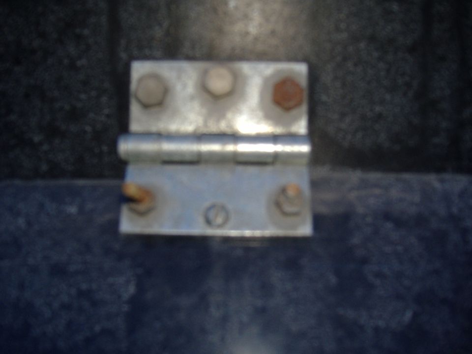 Close-up of a metal door hinge with bolts on a dark surface