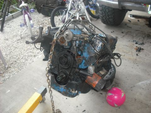 1982 Ford Bronco - Engine block being worked on, with chains attached for lifting and an engine stand supporting it.
