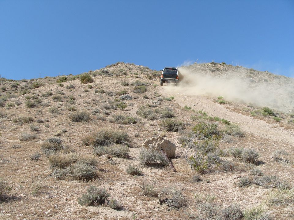 1995 Ford Bronco driving up a dusty desert hill, kicking up a cloud of dirt