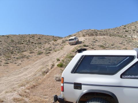 1995 Ford Bronco - Two white SUVs navigate a steep, dusty incline under a clear blue sky.