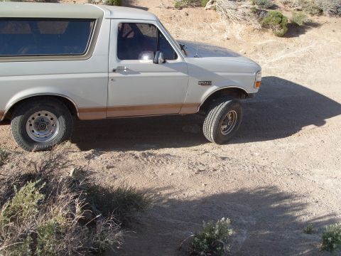 1995 Ford Bronco - A white Ford Bronco is parked on a dirt road in a dry, arid environment.