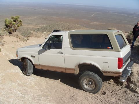 1995 Ford Bronco - A white 1995 Ford Bronco with a tan top is parked on a dirt road in a desert landscape.