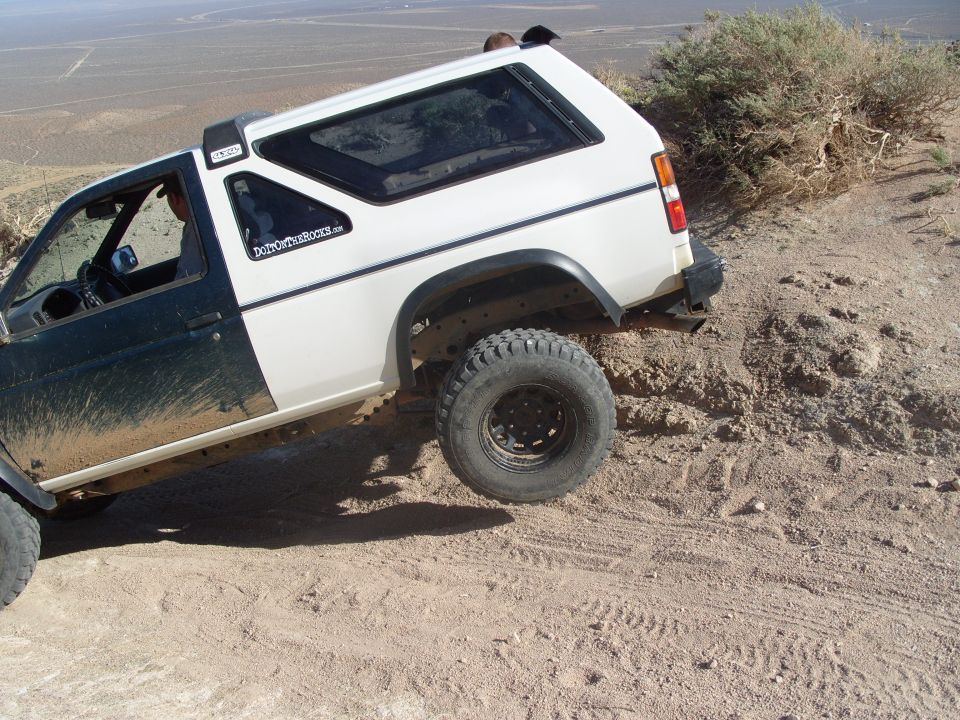 Two-tone SUV with off-road tires climbing a dirt hill. Sticker on door reads 'DirtCoversTheRest.com'