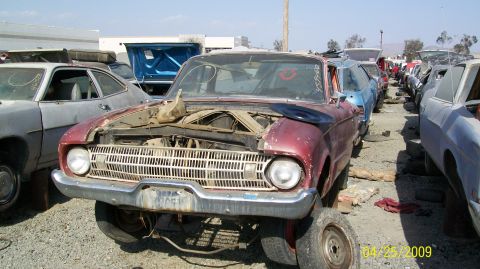 1972 Ford Ranchero - A front 3/4 view of a weathered, maroon classic car with its hood open, parked in an outdoor vehicle junkyard. The car's grille and headlig…