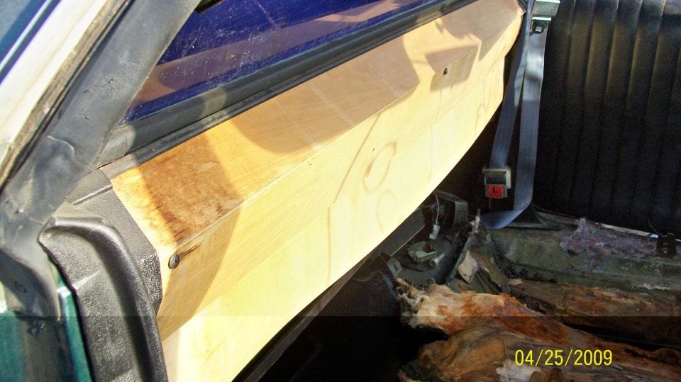 Interior view of a vehicle showing a custom wooden panel and a black seat with a seatbelt.