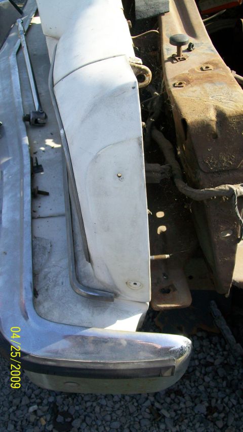 1972 Ford Ranchero - A close-up view of the front corner of a white vehicle's bumper and fender assembly, with a rusty metal frame visible to the right. The dat…