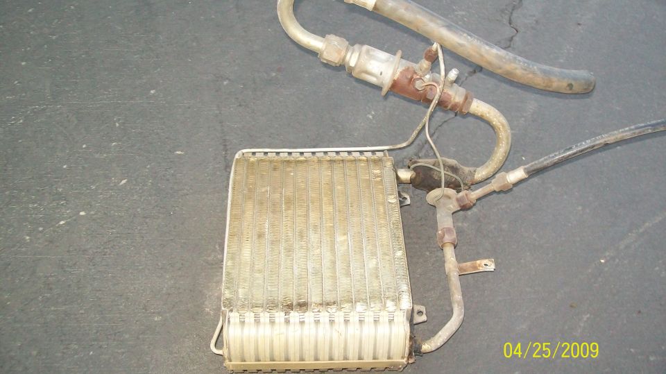 Car AC evaporator core with hoses on a dark surface.
