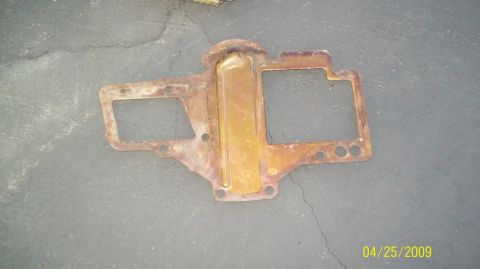 1972 Ford Ranchero - A rusty, golden-brown metal part with rectangular cutouts and mounting holes is shown from a top-down perspective on a cracked concrete sur…