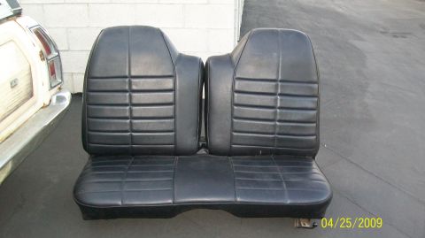 1972 Ford Ranchero - A pair of black vinyl bucket seats with a center console sits on a dark gray asphalt surface. To the left of the seats is the rear section…