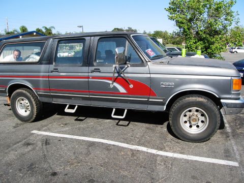 1986 Ford Bronco - Side view of a gray late-1980s Ford F-250 crew cab with red and silver swoosh graphics down the doors, a matching camper shell over the bed…