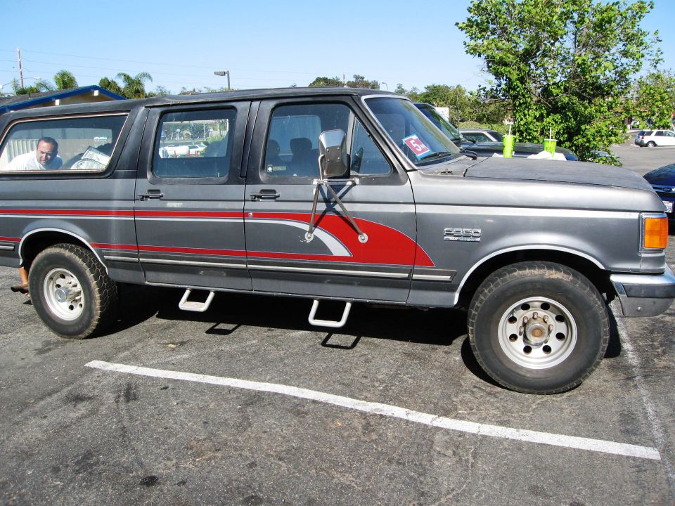 Gray 1980s Ford F-250 crew cab with camper shell, red swoosh stripes and tow mirrors